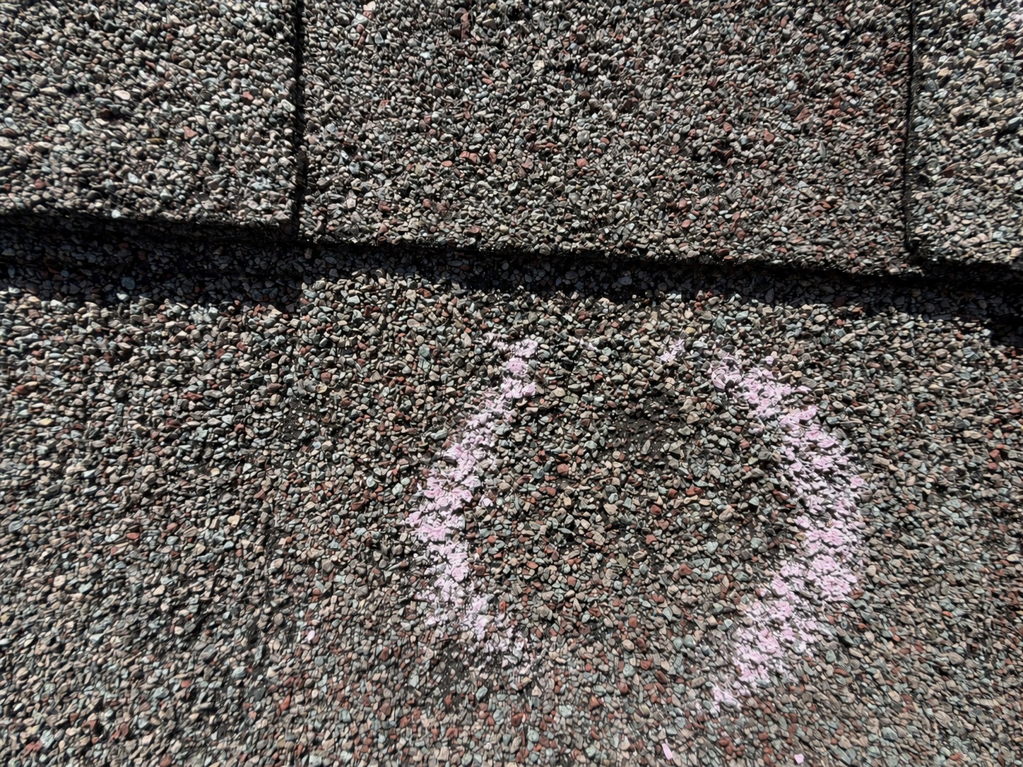 Close-up roof inspection photograph with chalk-marked suspected hail impacts